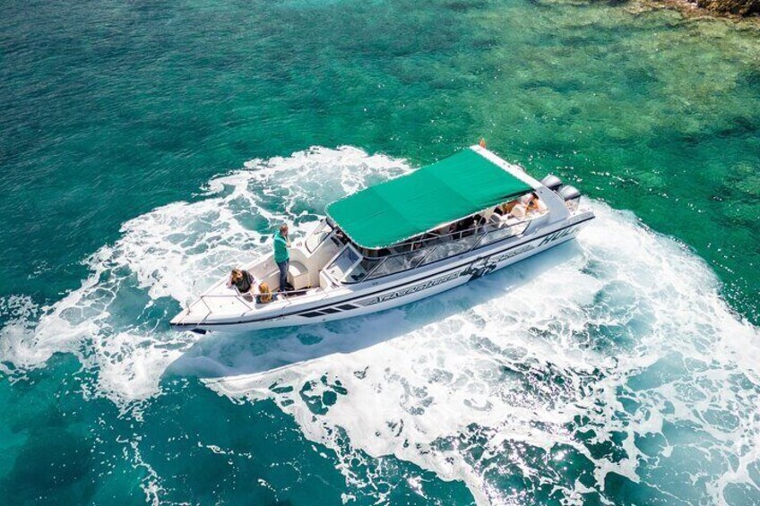 A boat with a green canopy, passengers, and a wake in turquoise water. 4