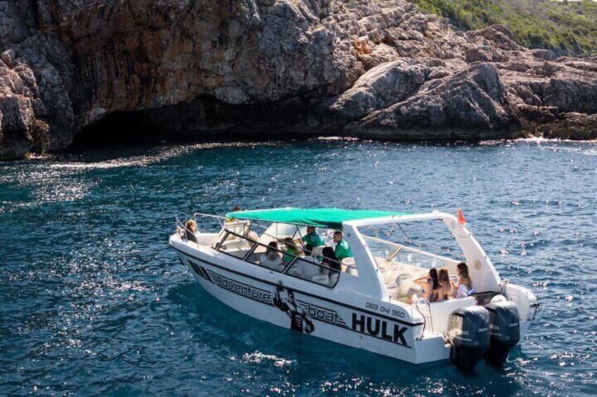A boat named 'HULK' with passengers, sailing near rocky cliffs. 5