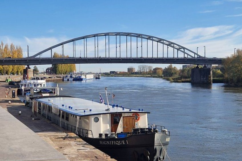 A river with a bridge, a boat docked at the pier, and a cityscape in the background. 2