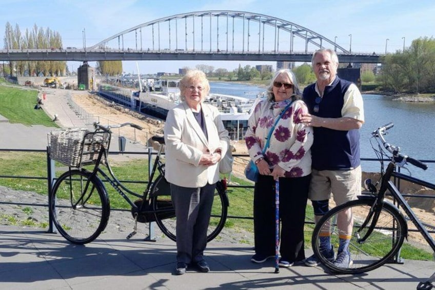 Three people standing by a river with a bridge in the background. 4