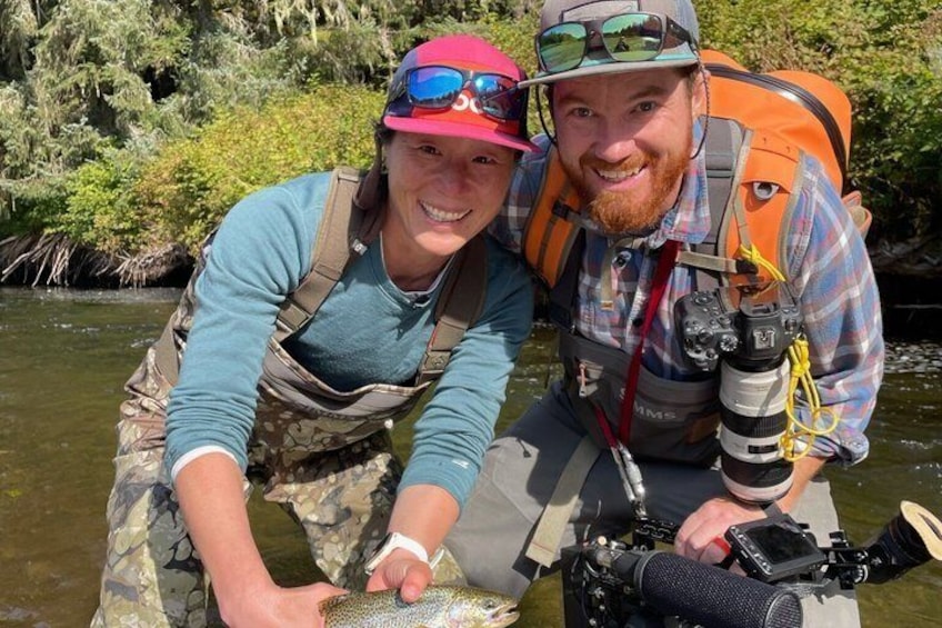 Deux personnes dans une rivière, l’une tenant un poisson, et l’autre portant un appareil photo. 2