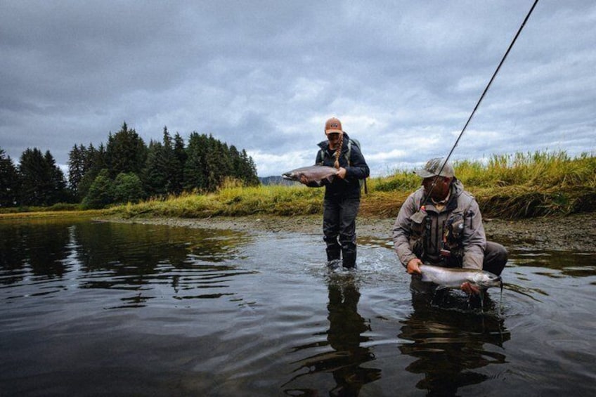 Deux personnes sont en train de pêcher dans une rivière, avec des arbres en arrière-plan. 1