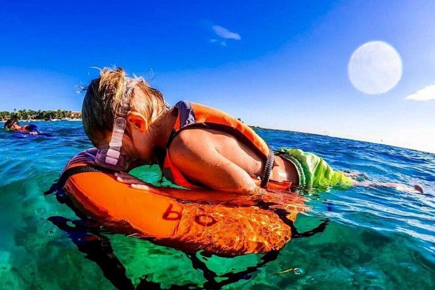 A person floating on water with a life jacket, clear blue water, and a bright sun in the sky. 2