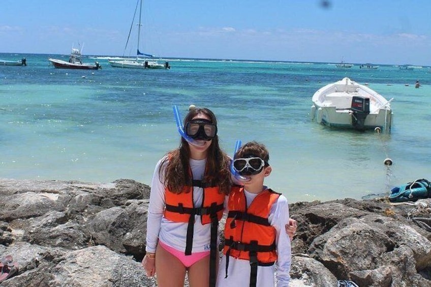 Two people wearing life vests and snorkeling gear on a rocky beach with boats in the water. 5