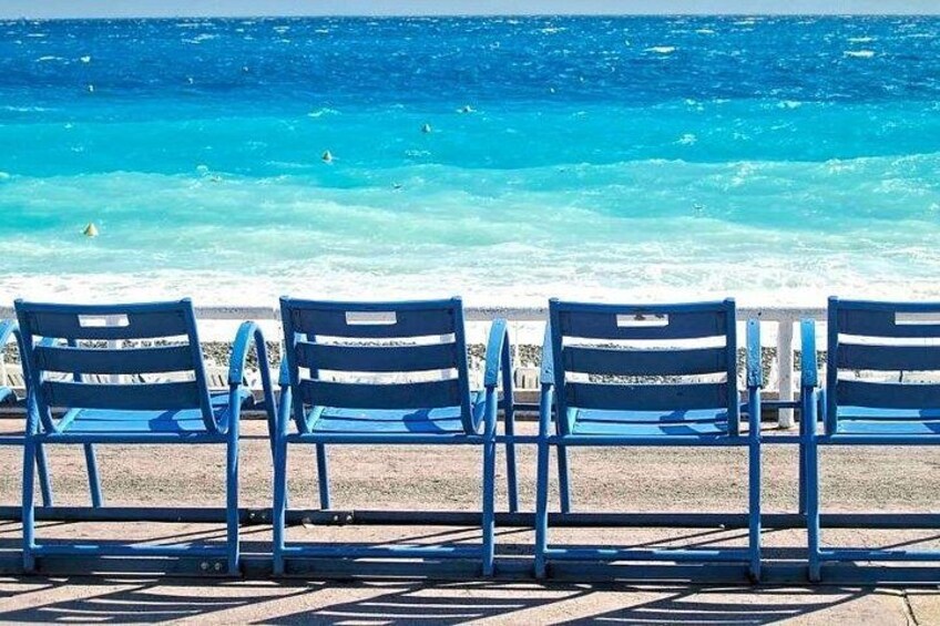 Filea di sedie blu rivolta verso una spiaggia con acque cristalline color turchese. 2
