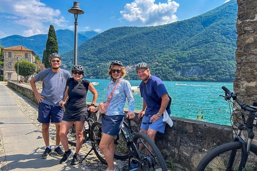 Un groupe de personnes se tient au bord de l’eau, à côté de leurs vélos, avec un lampadaire et une montagne en arrière-plan. 1
