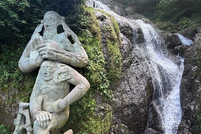 A waterfall cascading over moss-covered rocks with two stone sculptures of human figures. 2
