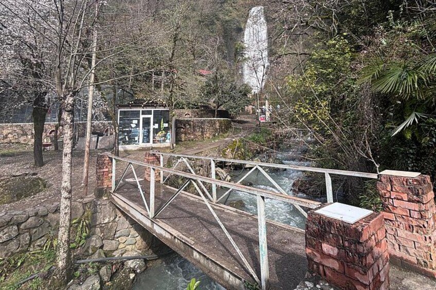 A stone bridge over a stream, surrounded by trees and a waterfall in the background. 5