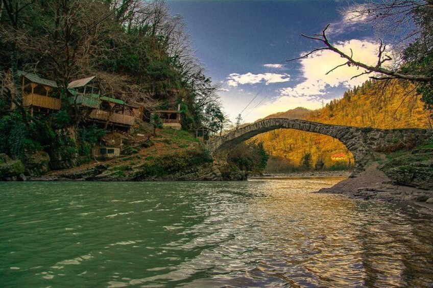 A stone bridge over a river, surrounded by trees and buildings. 4