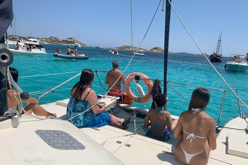 A group of people on a sailboat in a clear blue sea with other boats in the background. 5