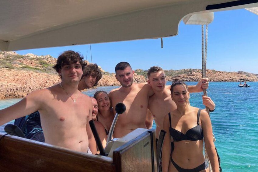 A group of people on a boat near a rocky shoreline with clear blue water. 2