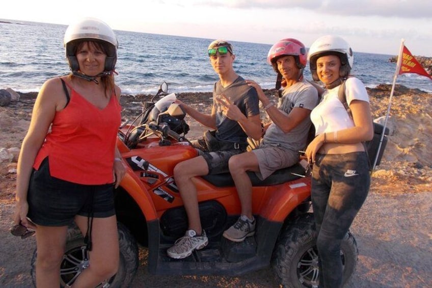 Vier Personen fahren mit einem Quad nahe einer felsigen Küstenlinie, im Hintergrund das Meer. 1