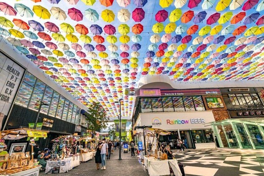 A covered market with colorful umbrellas, a Rainbow Beer store, and various shops. 2