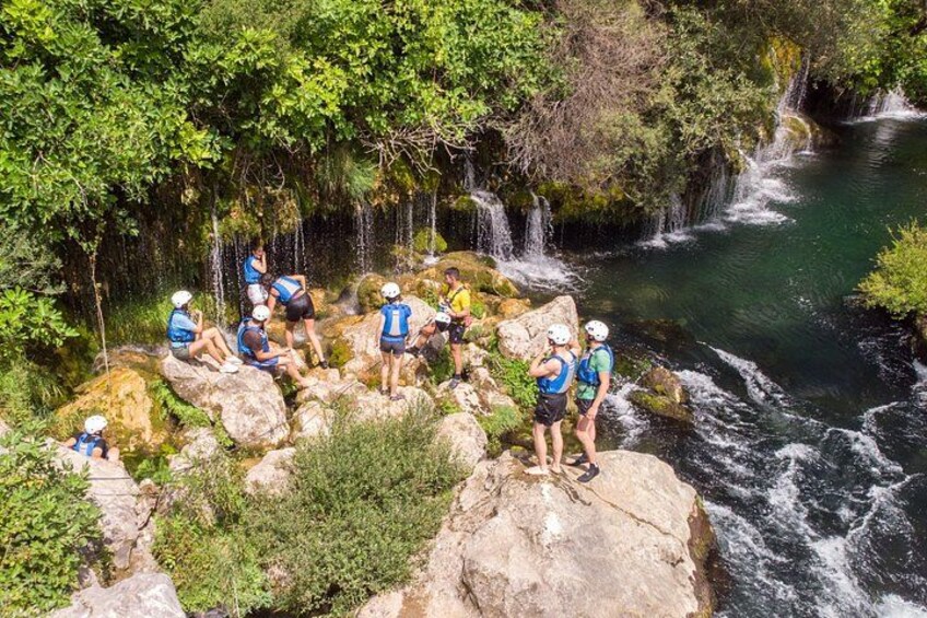 Un groupe de personnes, vêtues de chemises bleues et vertes, est assis sur des rochers près d’une cascade. 3