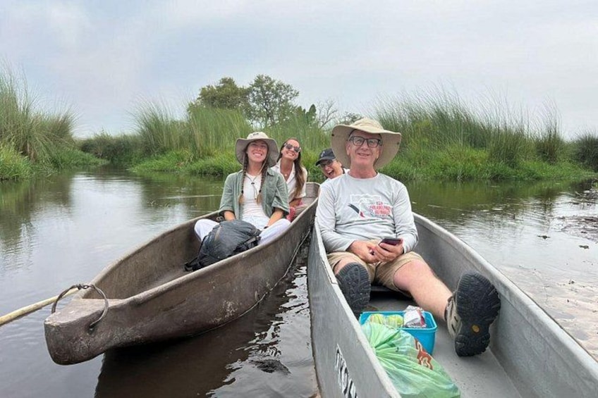 A group of people in a narrow waterway, surrounded by tall grass and trees. 2