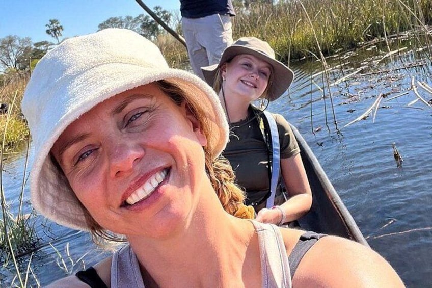 Two people in a canoe on a calm water body with reeds and trees in the background. 4