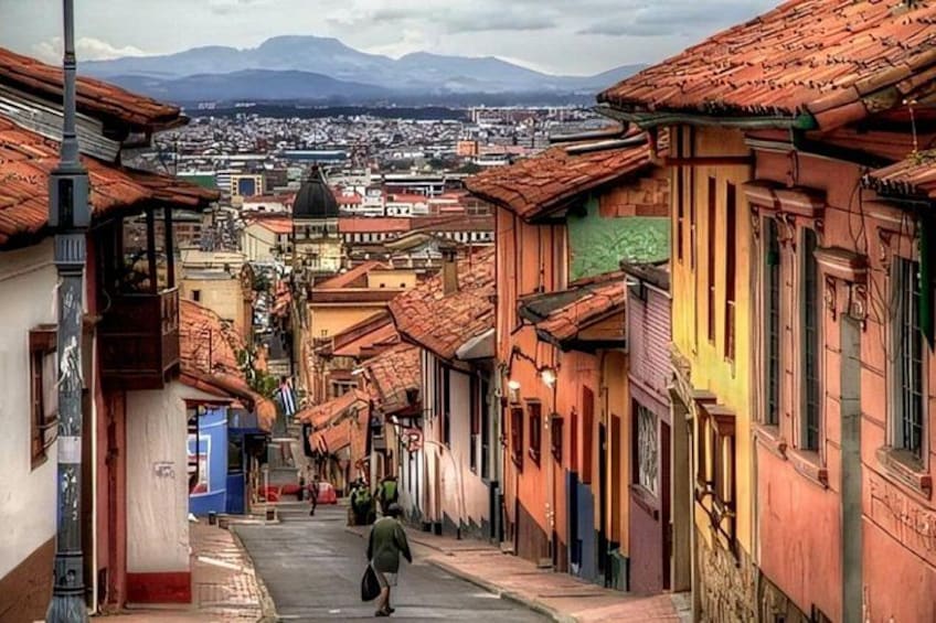 A narrow street with buildings, a person walking, and a mountain in the background. 2