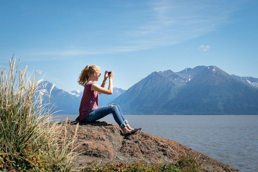 A person sitting on a rock by a lake with mountains in the background. 5