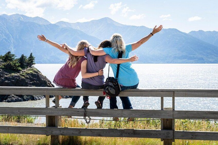 Three people embracing on a wooden railing overlooking a lake with mountains in the background. 4