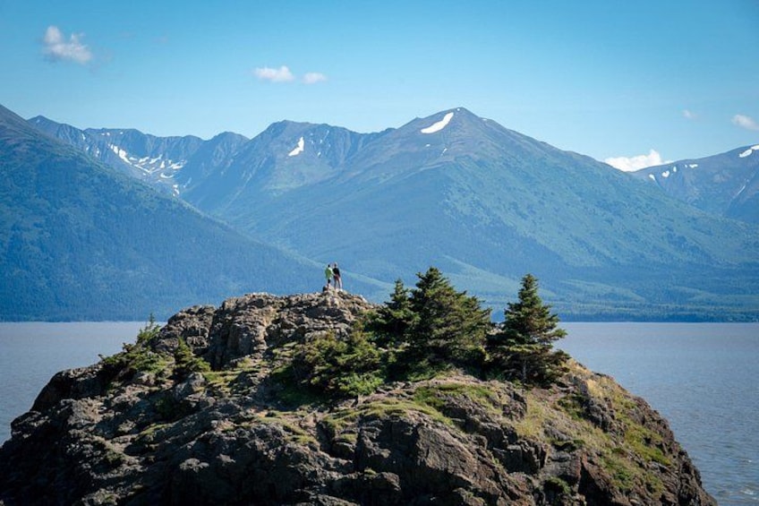 A person standing on a rocky island with a lake and mountains in the background. 2