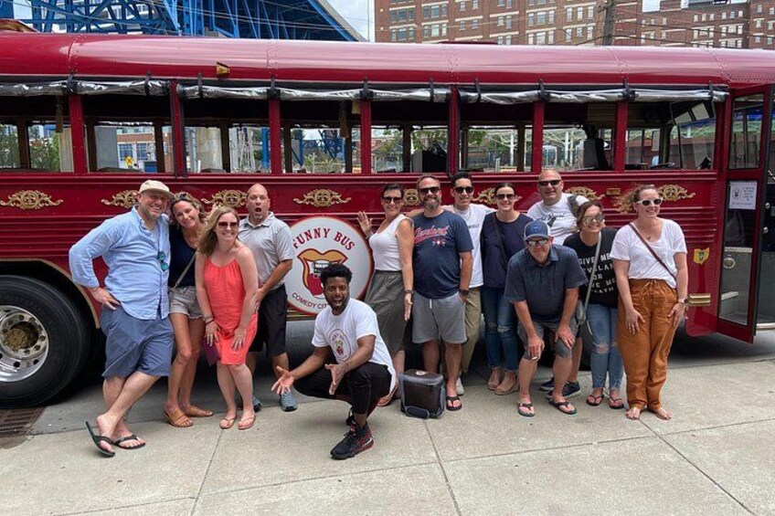 A group of people posing in front of a red bus with 'Funny Bus' written on it. 2
