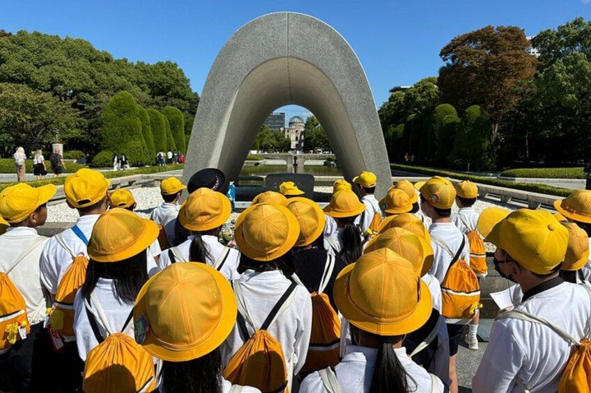 Un grupo de personas con sombreros amarillos y camisas blancas reunidas alrededor de un amplio arco de piedra en un parque. 2