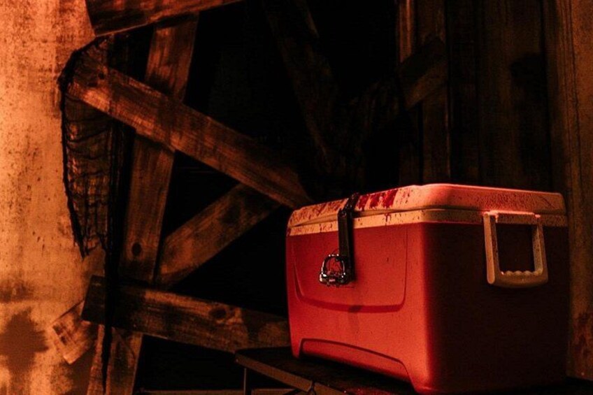 Une glacière rouge avec un loquet en métal, placée contre une structure en bois. 3