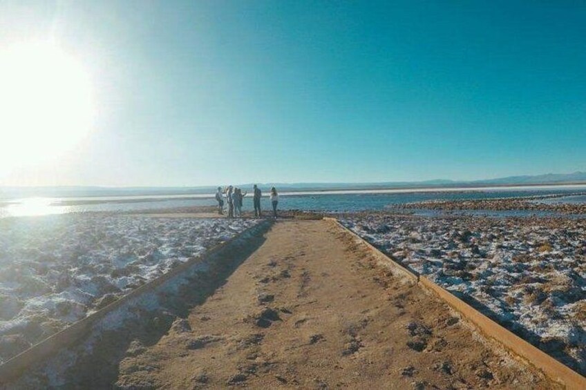 A beach with a concrete walkway, people standing on the sand, and a clear sky. 4