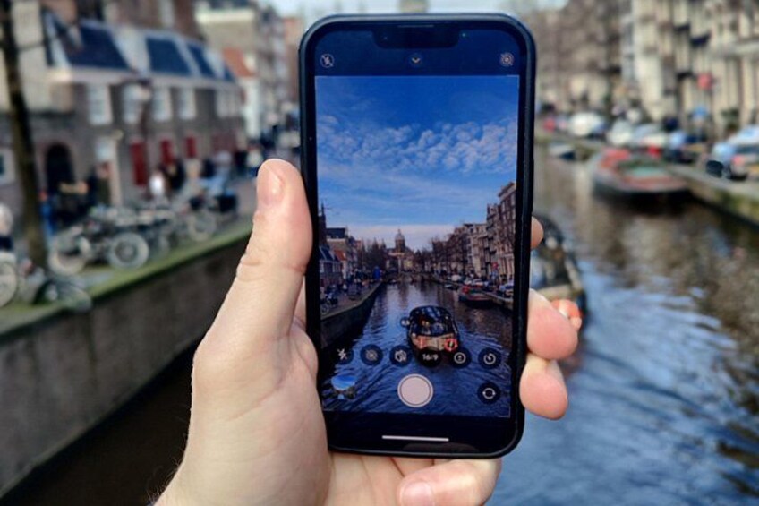A hand holding a smartphone displaying a canal scene with buildings and boats. 4