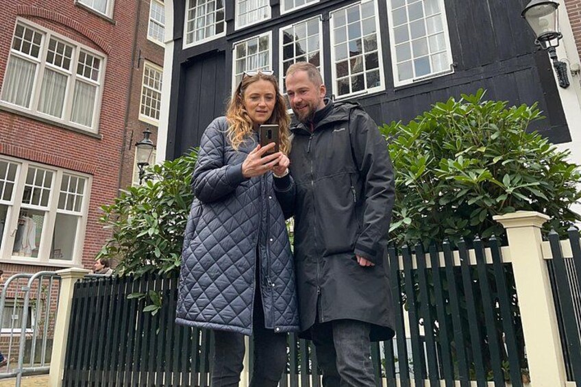 A person in a long coat standing next to a building with a black fence and greenery. 3