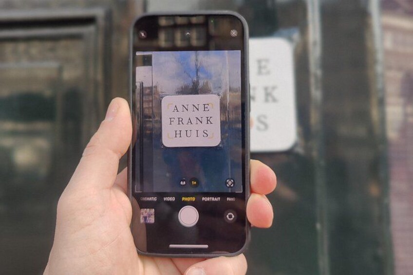 A hand holding a smartphone displaying a photo of a building with the name 'Anne Frank Huis' visible. 5