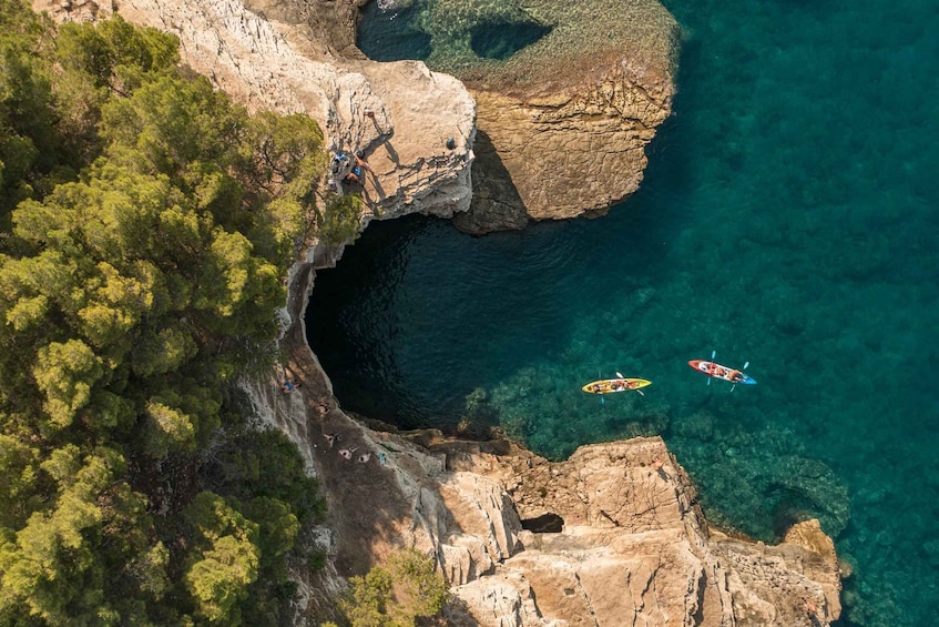 An aerial view of a coastal area with rocky cliffs, clear blue water, and kayaks. 1