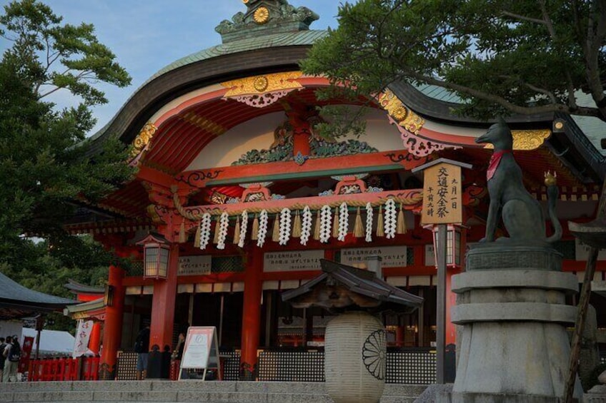 A traditional Japanese temple with a red and gold roof, a stone statue, and a sign with Japanese characters. 3