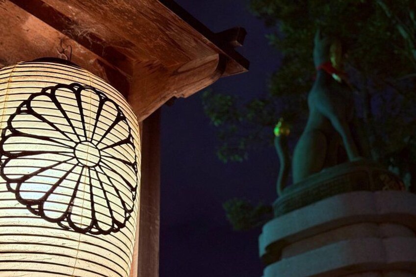 Escena nocturna con un farol encendido, una estructura de madera y una estatua de un gato. 3
