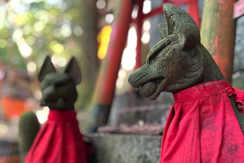Una estatua de piedra de un lobo vestido con una prenda roja, sobre un fondo borroso con una estructura roja. 4