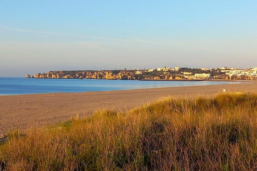 Eine Küstenlandschaft mit Sandstrand, grasbewachsenen Dünen und einer in der Ferne liegenden Stadt mit Gebäuden. 2