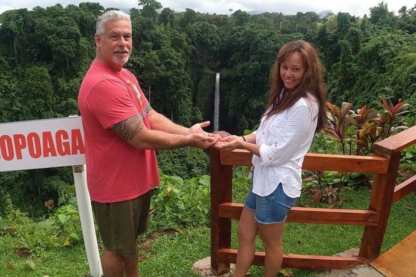 Two people shaking hands in front of a sign that reads 'OPOAGA' with a lush green forest in the background. 4