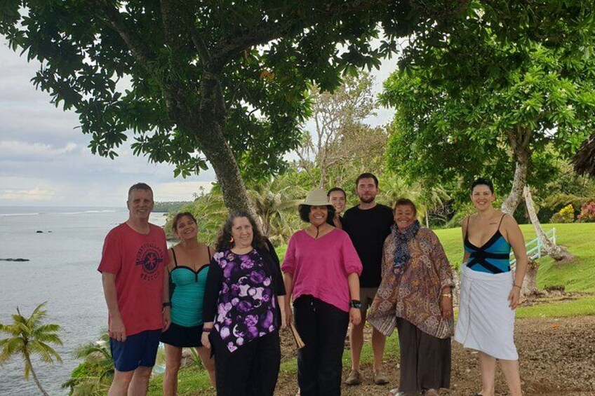 A group of people standing under a tree by a body of water. 2
