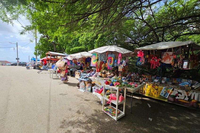 Outdoor market stalls with various goods, including toys and crafts, under a tree. 2