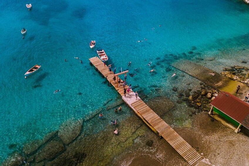 A wooden pier extending into a turquoise sea with boats and people. 5