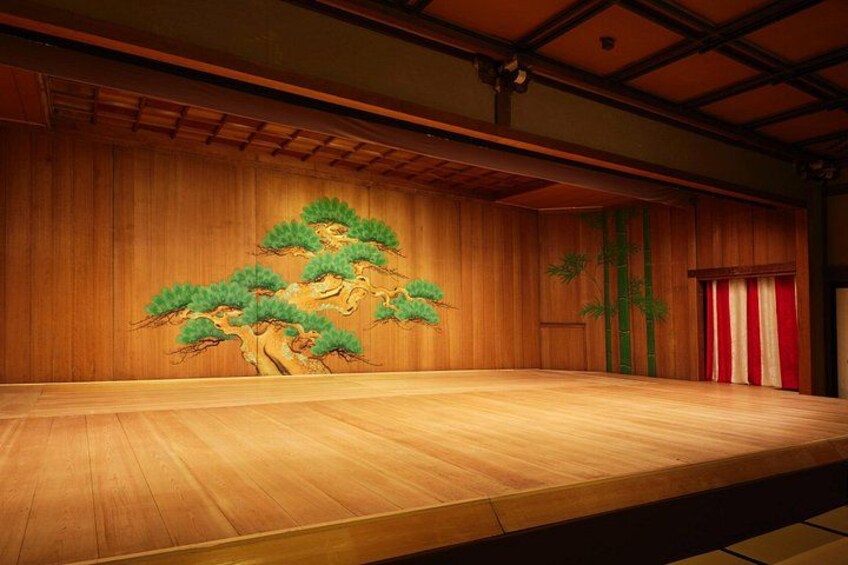 A stage with a wooden backdrop, a red curtain, and a painted tree. 4