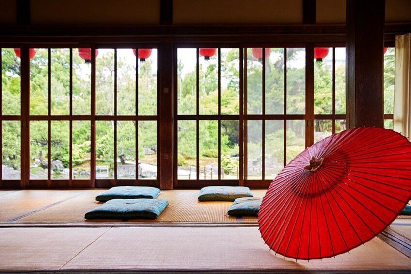 A traditional Japanese room with tatami flooring, a red folding screen, and a view of a garden through a shoji screen. 3