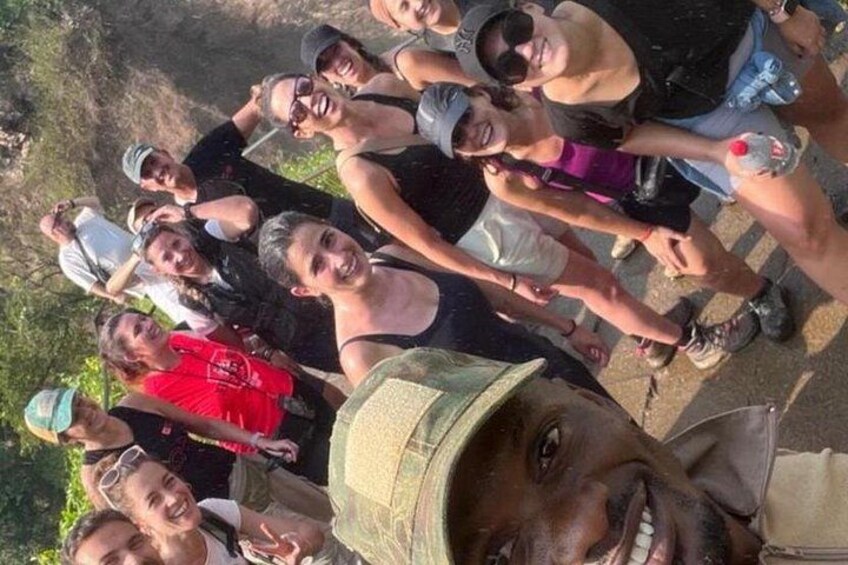 A group of people standing outdoors, some wearing hats and sunglasses, with a natural landscape in the background. 4