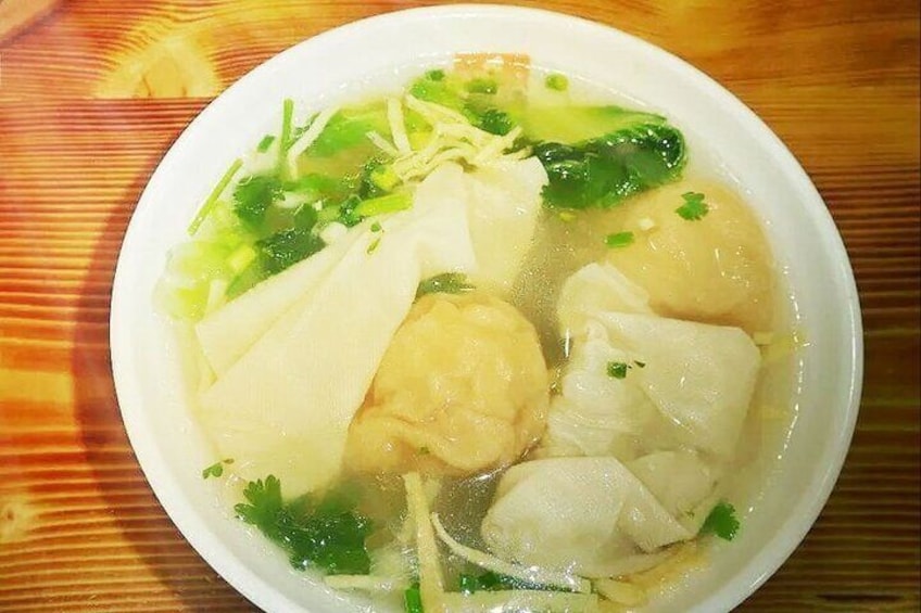 A bowl of soup with tofu, fish balls, and green vegetables. 3