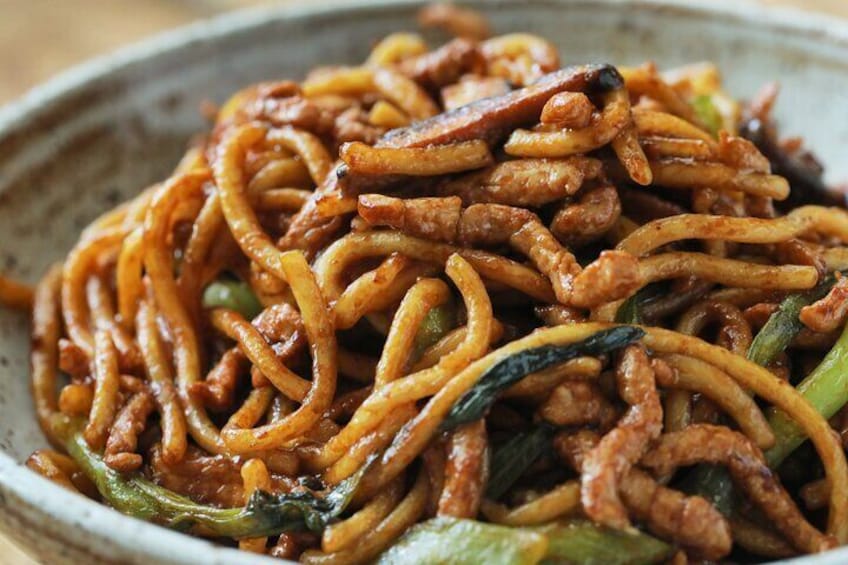 A bowl of stir-fried noodles with vegetables and meat. 4