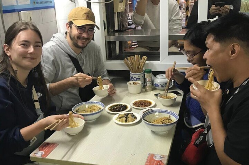 People sitting at a table eating noodles with chopsticks. 1
