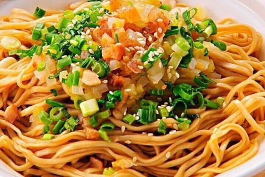 A bowl of noodles topped with chopped green onions, sesame seeds, and diced ingredients. 2