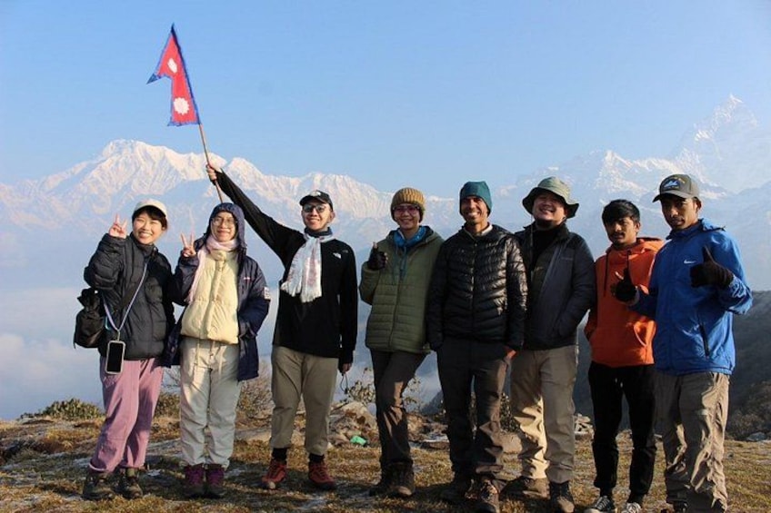 Un grupo de personas de pie en una montaña con una bandera, picos nevados al fondo. 1