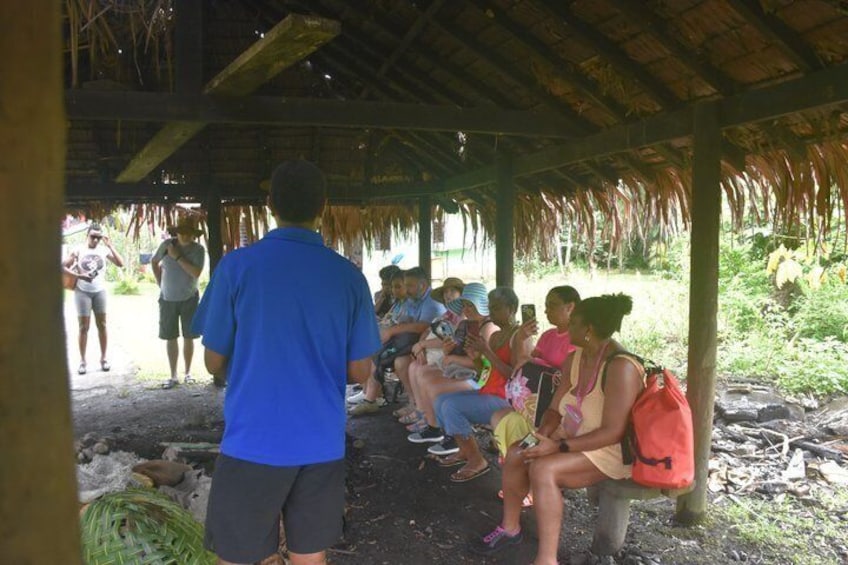 A group of people sitting under a thatched roof structure in a natural setting. 4