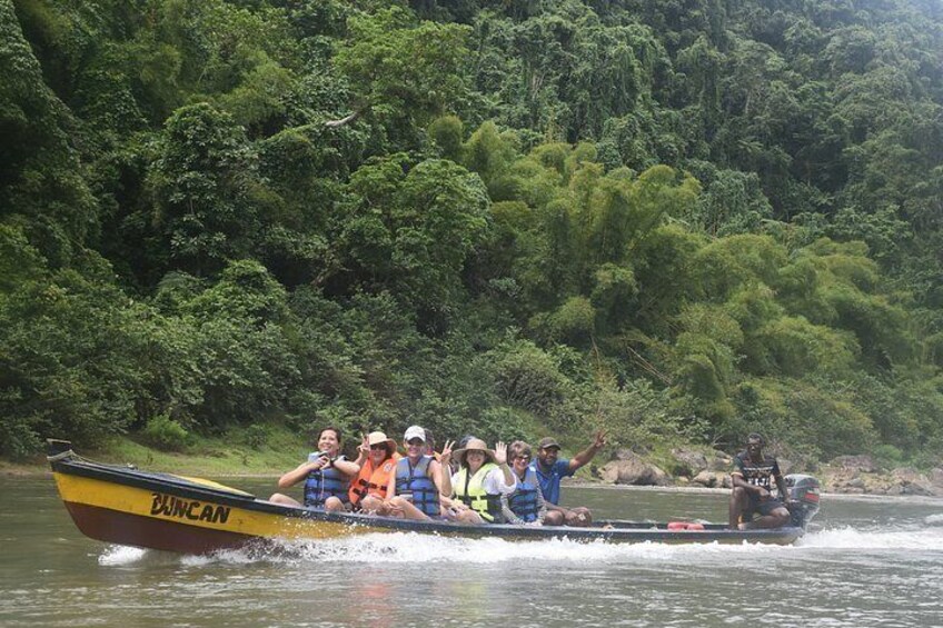 A group of people in a yellow boat labeled 'BUNCAN' on a river surrounded by dense green forest. 2